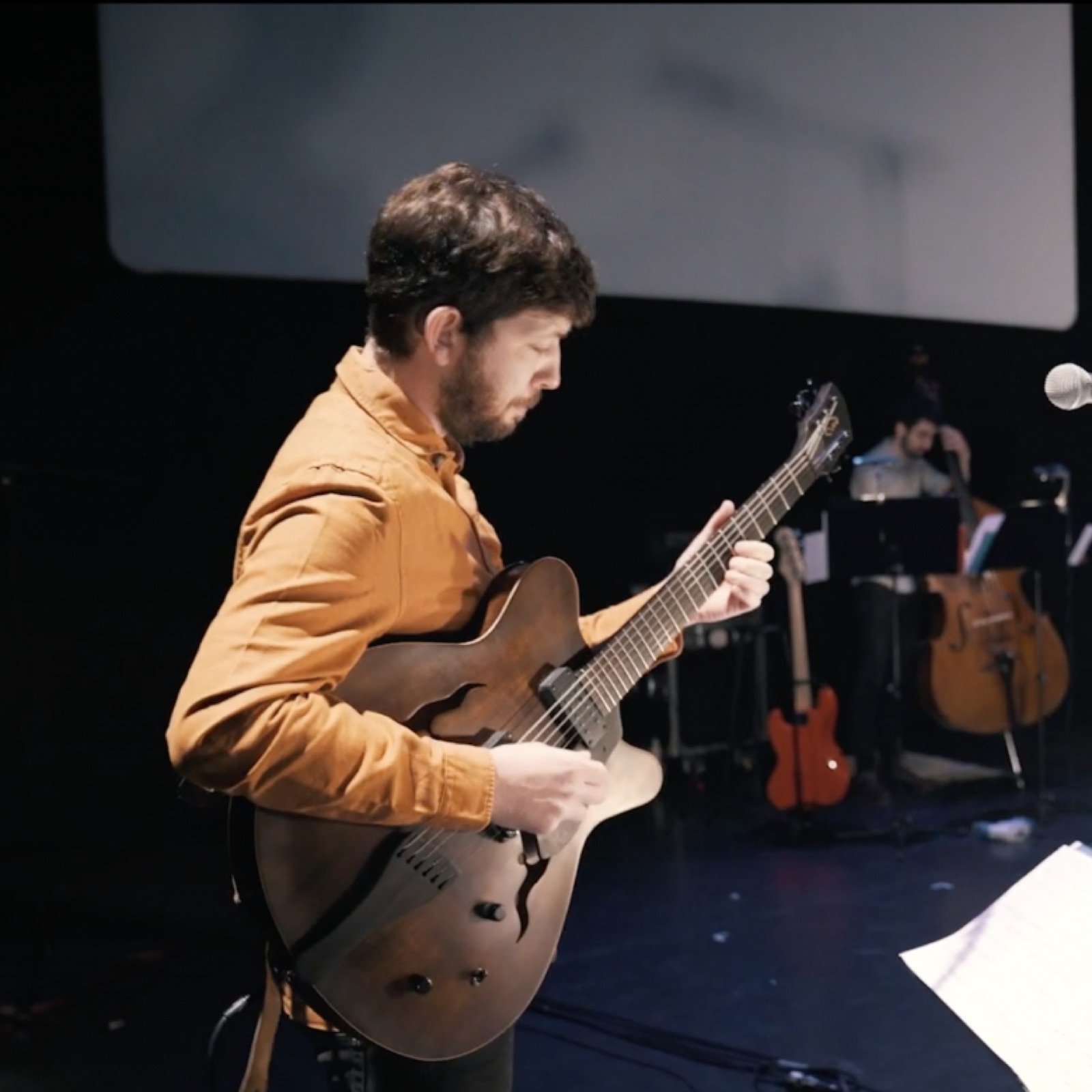 A guitarist in an orange shirt on stage during LULELA